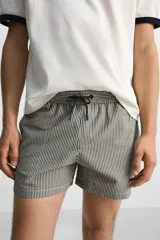 Short de baño con textura seersucker a rayas verticales azul marino y blanco. Tiene cintura elástica ajustable con cordón, bolsillos frontales y traseros, aberturas laterales en el bajo y forro interior.