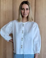Camisa blanca de lino con mangas 3/4 abullonadas con puños elásticos y cuello redondo con botones.