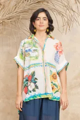 Camisa de manga corta con cuello clásico y cierre frontal con botones. Presenta un estampado con motivos florales, frutales y paisajes.