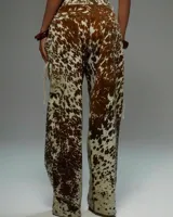 Conjunto de dos piezas (top y pantalón) con estampado que imita piel de vaca en tonos marrón y blanco. El top es tipo corset sin mangas, con cuello alto y lazada frontal ajustable. El pantalón es de tiro alto y corte recto.