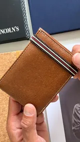 Billetera marrón de cuero liso con banda elástica tricolor. Interior con compartimento para billetes, visor y tarjeteros.