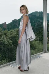 Vestido midi de tejido satinado color gris, con cuello halter, hombros descubiertos, abertura en el pecho, tirantes finos cruzados en la espalda y capa combinada a tono.