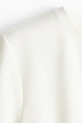 Remera blanca entallada de punto pesado interlock, con cuello redondo, mangas cortas, pinzas moldeadoras en la cintura y bajo acampanado.