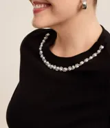 Blusa negra de algodón con cuello redondo y mangas cortas. Presenta aplicación de perlas artificiales y strass en el cuello.