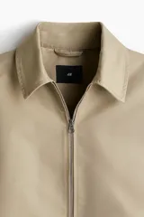 Campera color beige de denim rígido con cuello clásico, cierre frontal, bolsillos insertados al bies y un bolsillo interior. Elástico revestido en puños y bajo. Corte estándar y forrada.