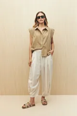 Camisa color beige, de corte recto, con cuello clásico, mangas cortas con volados en los hombros y cierre frontal con botones.