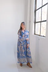 Vestido largo celeste con estampado floral en tonos beige, corte amplio, cuello camisero y mangas largas.