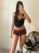 Top negro con escote drapeado, espalda descubierta y detalle de broche dorado en el hombro.