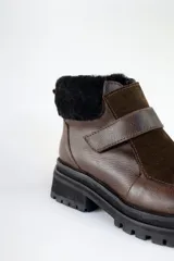 Bota corta de cuero color marrón con puntera y empeine de gamuza color beige. Tiene cuello de piel sintética color crema, cierre con velcro y suela track.