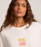 Remera alargada de algodón color crema con estampa de palmeras y atardecer en la playa.
