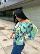 Blusa con estampado abstracto en tonos celeste, verde y azul, con escote off-shoulder, mangas abullonadas 3/4 con lazo y cintura elastizada con lazo.