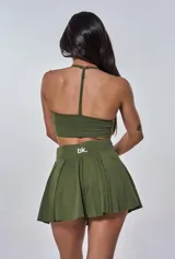 Conjunto deportivo verde militar compuesto por un top con breteles cruzados en la espalda y una minifalda plisada. El top tiene el logo 'bk.' estampado en blanco. Incluye calcetines blancos.
