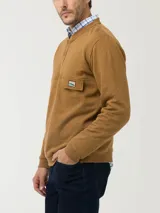 Buzo color ocre de algodón orgánico, con cuello redondo y abertura parcial con broches. Tiene un bolsillo tipo parche en el pecho con etiqueta RKF con paisaje bordado.