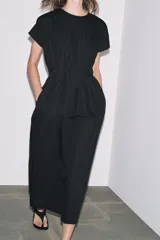 Vestido midi color marrón confeccionado en hilatura con mezcla de algodón y lino. Tiene cuello redondo, manga corta caída y detalle de pliegues en la cintura. Cierre en la espalda con abertura y botón.