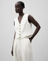 Chaleco corto color blanco, de lino y viscosa, con escote en pico, sin mangas, con botonadura frontal, bolsillos de vivo y pieza ceñidora con dos botones en la espalda.