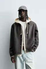 Cazadora de efecto piel color marrón oscuro, corte relajado, con cuello solapa, cierre frontal de botones a presión y bolsillos de vivo en cadera.