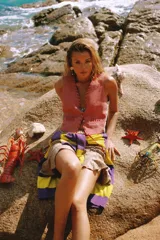 Chaleco de gamuza color beige con ribete rojo, cierre frontal con un botón y bolsillos laterales.