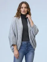Cardigan negro de tejido suave, estilo poncho o capa, con cuello tipo chal y mangas amplias.
