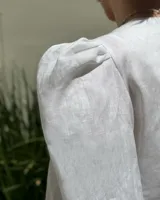 Blusa color rosa pálido de lino con bordados de motivos marinos, escote en V, mangas cortas abullonadas y cierre frontal con botones.