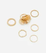 Set de seis anillos dorados de metal con diferentes diseños: uno con forma de flor, uno con textura trenzada, uno con textura de bolitas, uno con textura labrada, uno liso y uno con forma de rama.