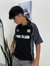 Chomba deportiva de manga corta, color negro en el frente y gris oscuro en las mangas. Tiene cuello polo negro y ribetes blancos que separan los colores. Presenta un estampado frontal con el número "00" y el texto "RANK CLUB" en blanco.