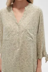 Blusa color beige con estampado de arabescos blancos, cuello mao, mangas 3/4 con lazos en los puños, cierre parcial con botones y bolsillos frontales.