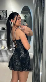 Vestido corto negro con breteles finos y falda evasé. Presenta un estampado de lunares plateados.