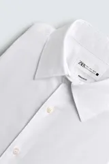 Camisa blanca de corte regular fit, con cuello italiano, manga larga con puños abotonados y cierre frontal con botones.