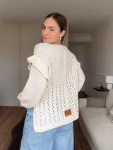 Sweater de punto calado color crema, con mangas largas y volados en los hombros. Tiene corte holgado y etiqueta de cuero con logo en la parte inferior.