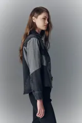 Campera recta de denim rígido negro con recortes en gris. Tiene bolsillos con solapa y botones metálicos.