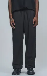 Pantalón deportivo negro de nylon con cintura elástica, cordón ajustable y aberturas laterales con broches a presión.
