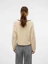 Cardigan tejido color crema con cuello polo, cierre con botones negros y ribete negro con forma de ondas en cuello, cierre, bolsillos y ruedo.