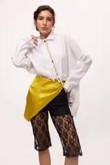 Camisa blanca de lino y algodón, con cuello clásico, cierre frontal con lazos y mangas largas abullonadas con puños ajustables con lazos.