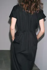 Vestido midi color marrón confeccionado en hilatura con mezcla de algodón y lino. Tiene cuello redondo, manga corta caída y detalle de pliegues en la cintura. Cierre en la espalda con abertura y botón.