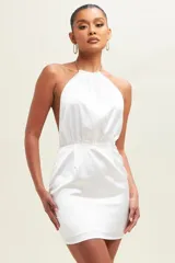 Vestido corto blanco de satén con escote halter con cadena dorada y espalda descubierta.