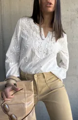 Blusa blanca de algodón con bordado broderie, escote en V y mangas largas.
