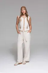 Conjunto de chaleco y pantalón de lino color crudo con bordados artesanales en tono beige. El chaleco es sin mangas con terminaciones decorativas en la vista frontal. El pantalón es de tiro alto, corte recto y caída relajada, con cintura con lazo ajustable y detalles en madera.