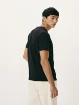 Camiseta blanca de algodón con cuello redondo y mangas cortas. Estampa rectangular con borde negro que contiene la frase "NATURAL ATMOSPHERE" en letras mayúsculas y una imagen de montañas y mar.