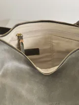 Bolso tipo bandolera de cuero color verde oliva, con textura suave y acabado desgastado. Presenta un diseño curvado y amplio, con correa ajustable sujeta con hebillas y pasadores de cuero de color más claro. El interior está forrado y cuenta con tres bolsillos.