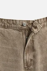 Pantalón color marrón con efecto lavado, corte relaxed fit, cinco bolsillos, aplicación de tira y bolsillo multifunción en perneras, cierre frontal con cremallera y botón.