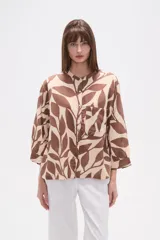 Camisa holgada con estampado de hojas en tonos marrones y beige, cuello mao, cierre frontal con botones y un bolsillo en el pecho.