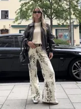 Pantalón de jean blanco con estampado de manchas negras, corte acampanado y tiro alto.