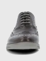Zapato tipo Oxford o Brogue de cuero marrón oscuro, con puntera y laterales decorados con perforaciones (broguing). Posee cordones grises y una suela deportiva gruesa de goma color gris claro.
