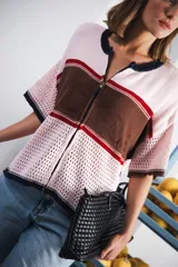 Remera de tejido calado color crudo con rayas horizontales rojas y terminaciones marrones, con cierre frontal y logo bordado.