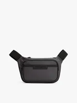 Riñonera negra de poliéster con acabado liso y logo metálico de Tommy Hilfiger en el frente. Cuenta con cierre de cremallera, cartera ajustable, compartimento principal y bolsillo exterior con cremallera.