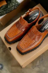 Zueco negro con textura croco, diseño tipo mocasín y tira regulable al talón.