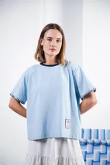 Remera celeste de algodón con cuello redondo a contratono azul marino, mangas cortas con detalle de bordado a mano y parche bordado en el frente inferior izquierdo. Corte recto y hombro caído.