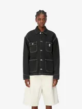 Campera de jean celeste claro, estilo abrigo de trabajo, con cuatro bolsillos delanteros, cierre de botones metálicos grabados con el logo de Carhartt y etiqueta con logo en el bolsillo del pecho.