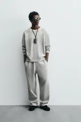 Pantalón de jogging gris con corte relaxed fit, cintura elástica ajustable con cordón interior, bolsillos laterales y traseros de vivo, y banda lateral color crema.