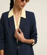 Blazer azul marino de corte sastrero, con solapas con detalle de puntilla en color crema, cierre con un botón dorado y bolsillos delanteros con solapa.